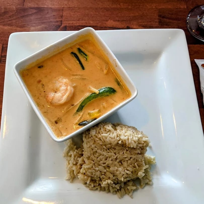 Thai red curry with shrimp and vegetables in a white bowl, served with brown rice.