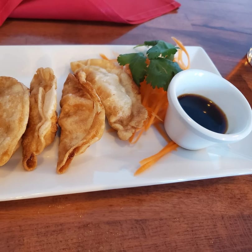Crispy fried Thai dumplings with a side of soy sauce, garnished with cilantro and shredded carrots.