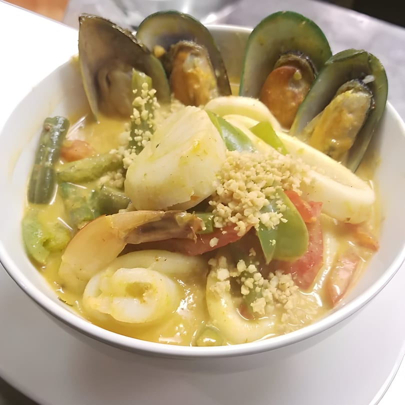 Thai seafood curry with mussels, shrimp, squid, and vegetables in a white bowl.
