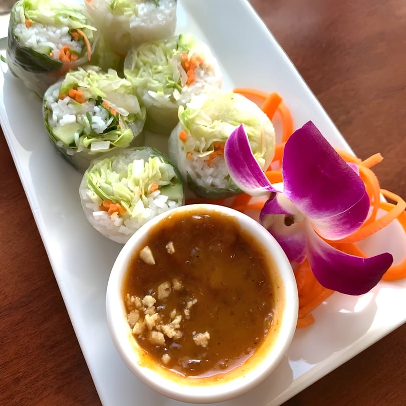 Fresh spring rolls with rice, lettuce, and carrots, served with peanut sauce and an orchid.