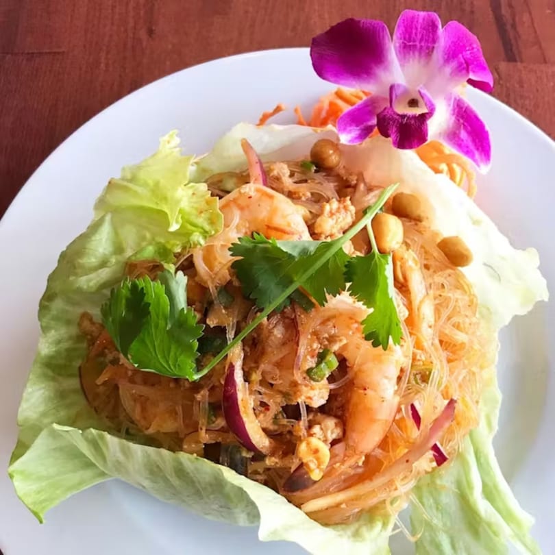 Thai glass noodle salad with shrimp, peanuts, red onion, and cilantro, garnished with an orchid.